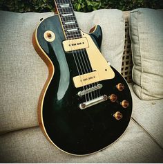 a black electric guitar sitting on top of a couch next to a green planter