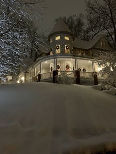 a large house is lit up at night in the snow with christmas wreaths on the porch