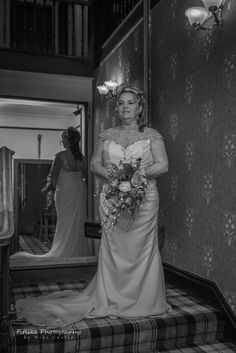 a woman standing in front of a mirror wearing a wedding dress and holding a bouquet