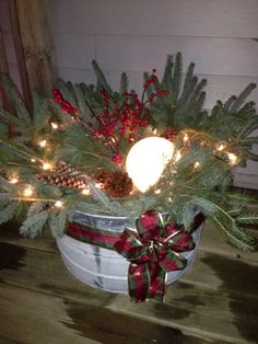 a christmas arrangement in a bucket with lights and pine cones on the top, sitting on a porch