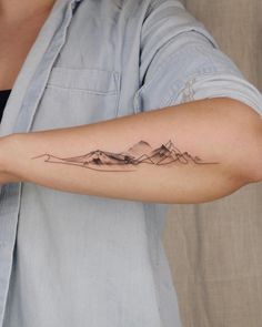 a woman's arm with a mountain tattoo on the left side of her arm