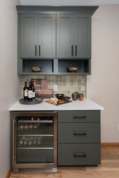 a kitchen with gray cabinets and white counter tops, wine bottles on the top shelf