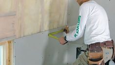 a man in white shirt working on a wall with tape and window frame attached to it