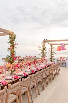 a long table set up with pink flowers and greenery on the tables for an outdoor wedding reception