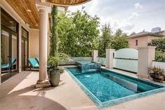 an outdoor swimming pool surrounded by plants and trees with blue chairs on the patio next to it