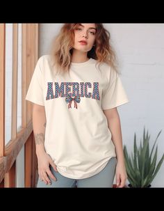 Introducing our Patriot Pride T-Shirt, the perfect blend of style and American spirit! This striking t-shirt features the word "AMERICA" emblazoned in bold, block letters, each filled with a pattern of white stars against a deep blue background. Reminiscent of the starry field of the American flag, these stars shine brightly, symbolizing the unity and strength of our nation. The letters are outlined in vibrant red, adding a bold and patriotic touch to the design. But that's not all - below the central part of the text, a decorative bow steals the spotlight. Mimicking the iconic design of the American flag, this bow features stripes in bold red and crisp white, while a blue field adorned with white stars completes the look. It's a nod to the timeless symbol of American freedom and pride. Cr American Freedom, Patriotic Tees, American Spirit, Pride Tshirts, American Pride, Block Lettering, Vibrant Red, Shirt Price, Fabric Color