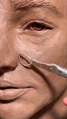 a person with a pair of scissors in their hand next to a clay face that is being sculpted