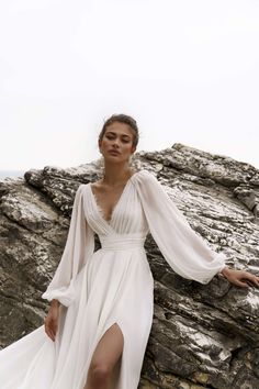 a woman in a white dress leaning against a rock