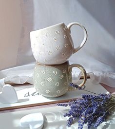 two mugs sitting on top of each other next to lavender flowers and spoons