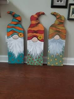 three painted wooden gnomes sitting on top of a hard wood floor next to a wall