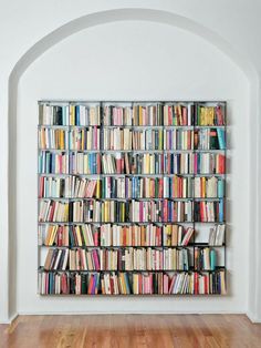 a book shelf filled with lots of books on top of a hard wood floor next to a white wall