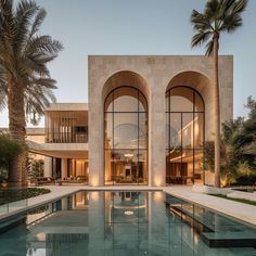 an outdoor swimming pool in front of a large building with arched windows and palm trees