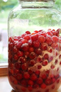 a jar filled with red berries sitting on top of a wooden table next to a window