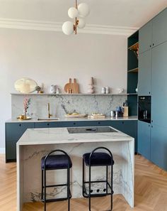 two stools sit in front of an island with marble countertops and blue cabinets