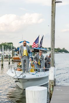 two men in suits stand on the bow of a small boat as others look on