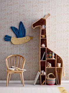 a giraffe made out of cardboard sitting next to a chair and wallpaper