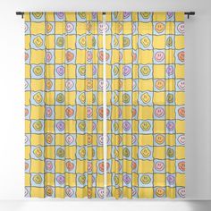 a window curtain with smiley faces on yellow and blue squares in the center, hanging from a white wall