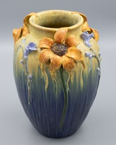 a yellow and blue vase with flowers painted on the outside of it's body