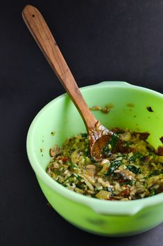 a green bowl filled with food on top of a black table next to a wooden spoon