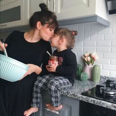 a mother and her daughter sharing a kiss in the kitchen while drinking from a cup