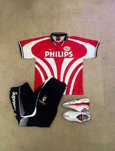 a red and white soccer uniform sitting on top of a floor next to other items