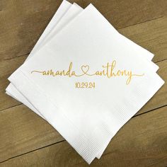 three personalized napkins with gold ink on them sitting on a wooden table top