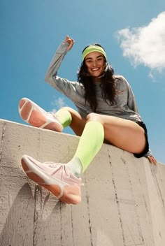 a woman sitting on top of a cement wall with her legs crossed and wearing tennis shoes