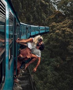 two people climbing up the side of a blue train with trees in the back ground