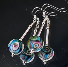 three glass bead earrings hanging from a metal hook on a black background with silver earwires