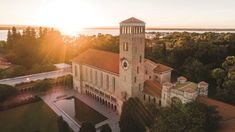 an aerial view of a building with trees surrounding it and the sun setting in the background