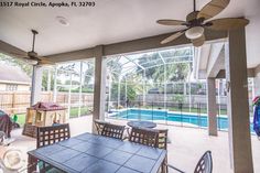 an enclosed patio with table, chairs and ceiling fan in the middle of it that overlooks a swimming pool