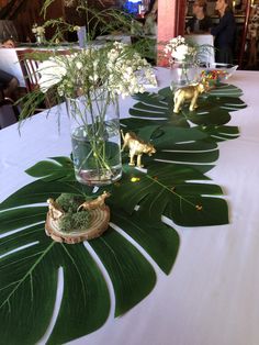 the table is set up with green leaves and vases filled with white flowers, small giraffe figurines on each side