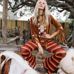 a woman sitting on top of a wooden bench next to a llama in front of a tree