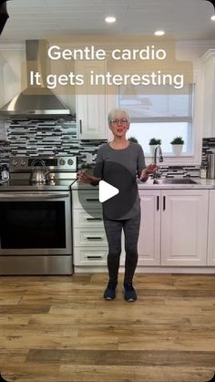 a woman standing in front of a stove top oven next to a kitchen with white cabinets