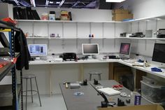 a room filled with lots of desks and computer monitors on top of white shelves