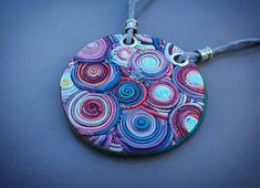 a circular pendant is decorated with colorful circles on a gray cord and hangs from a black cord