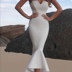 a woman standing on top of a sandy beach wearing a white dress and high heels