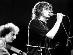 black and white photograph of two men singing into microphones while another man plays guitar in the background