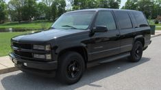 a black truck parked on the side of a road in front of a lake and trees