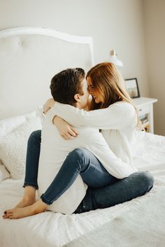 a man and woman sitting on top of a bed hugging each other while they are cuddling