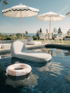 an inflatable lounge chair next to a pool with chairs and umbrellas around it