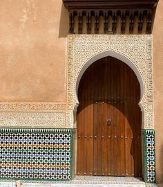 an ornate doorway with a wooden door and decorative tile work on the wall behind it