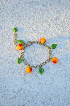 an orange and green bracelet with leaves on it sitting on the ground next to sand