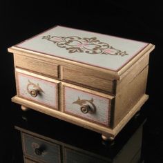 a small wooden box with two drawers on the front and one drawer open to show an ornate design