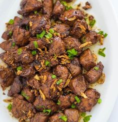 a white plate topped with meat covered in sauce and garnished with green onions