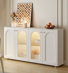 a white cabinet with two doors and some fruit on top, in front of a window