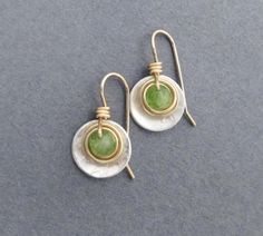 Faceted green genuine peridot gemstones, weighing 1.25 carats each, are wrapped in gold filled wire, then set within a sterling disc dangle. Ear hooks are handcrafted in gold filled wire. Artisan elegance and lightweight design make these earrings perfect for all day wear and comfort. Also are a great gift for a special someone with an August birthday, as peridot is August's birthstone. Genuine peridot, 1.25 carats each (2.5 carats per pair), pale green with natural inclusions visible. Earring D Lime Green Birthstone Jewelry For Anniversary, Anniversary Lime Green Birthstone Jewelry, Green Peridot Drop Earrings, Teardrop Peridot Jewelry For Anniversary, Elegant Green Hammered Earrings, Green Peridot Earrings For Anniversary, Green Sterling Silver Hammered Jewelry, Green Hammered Sterling Silver Jewelry, Lime Green Jewelry With Matching Earrings For Gift