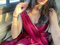 a woman sitting in the back seat of a car wearing a red sari and holding her hand up to her ear