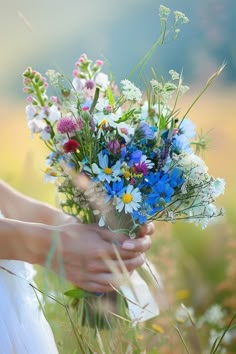 a woman holding a bouquet of wildflowers in her hands and wearing a white dress