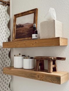 two wooden shelves with items on them in a bathroom next to a toilet paper dispenser